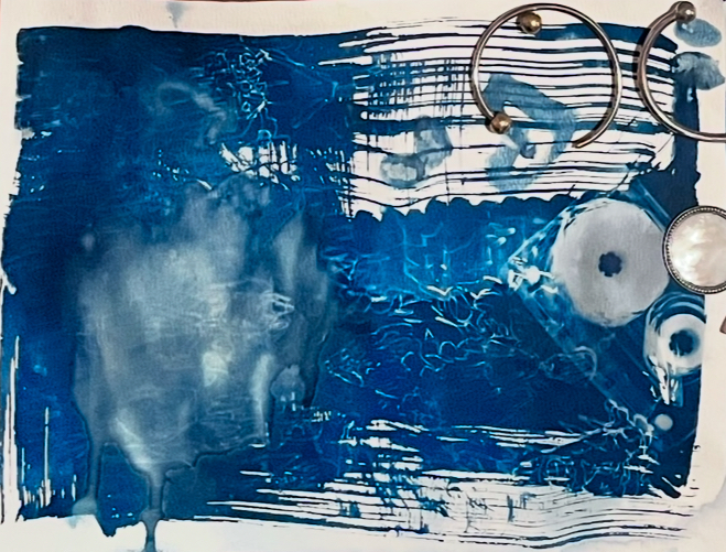Abstract cyanotype print in deep blue tones with white streaks and patterns, featuring metallic circular elements on the right side against a textured background.