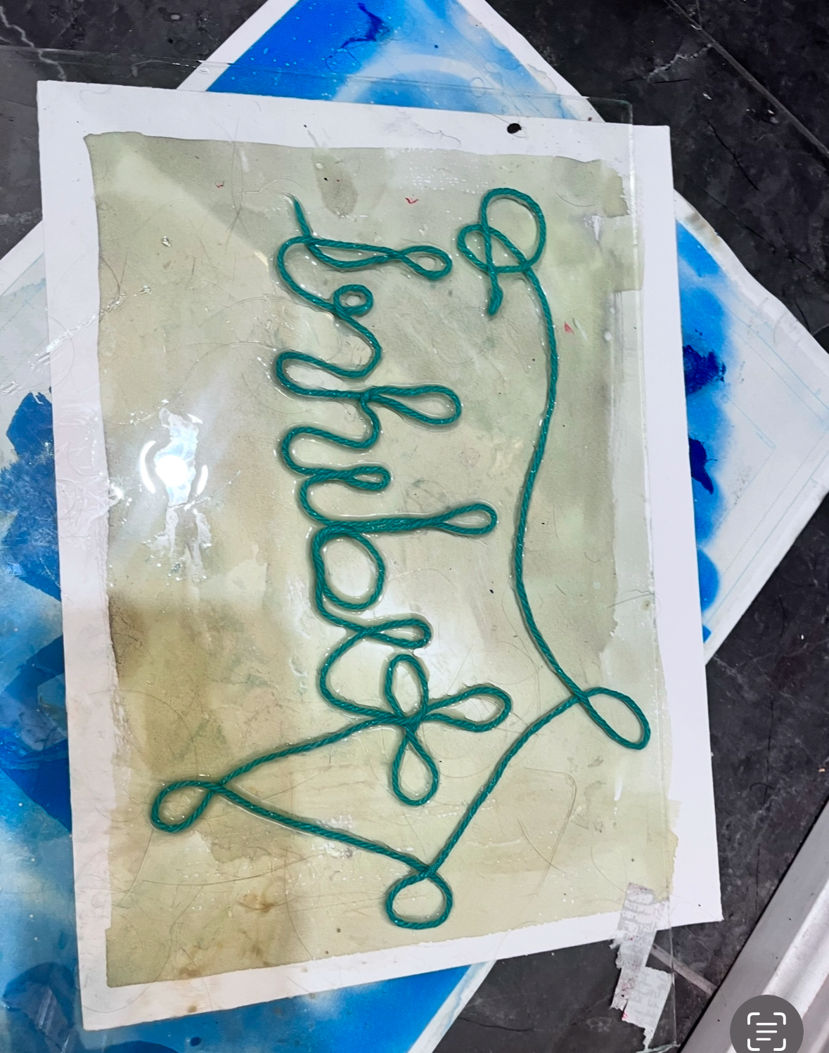 Artistic composition featuring teal thread arranged in a flowing, looping pattern against a pale green-yellow translucent background, creating an organic line drawing effect.