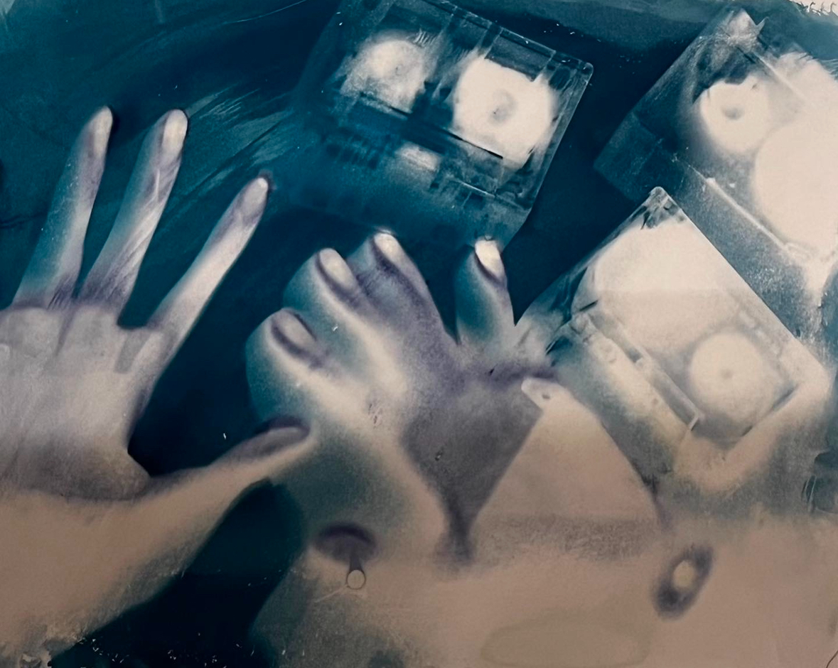 Cyanotype print showing ghostly hand silhouettes overlapping with circular objects, creating a mysterious, ethereal composition in deep blue tones with white highlights.