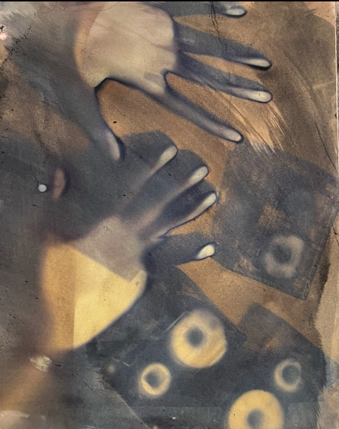 Experimental photographic print showing shadowy hand silhouettes against an earthy brown and gold textured background with circular elements, creating a dreamlike, tactile composition.