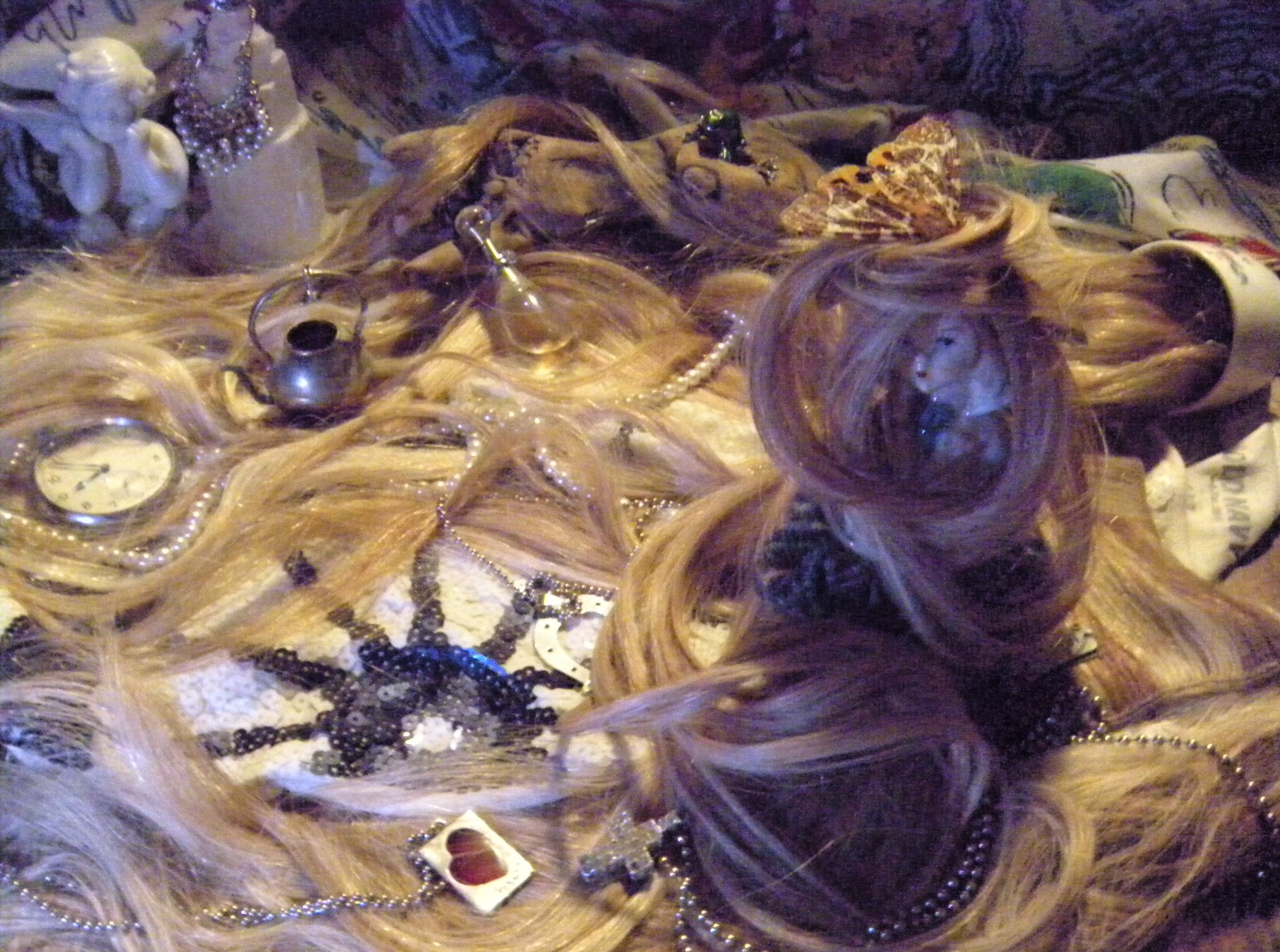 Artistic arrangement of blonde hair extensions interwoven with vintage objects including a miniature silver teapot, pocket watch, and beaded jewelry, creating a dreamlike composition against a dark purple background