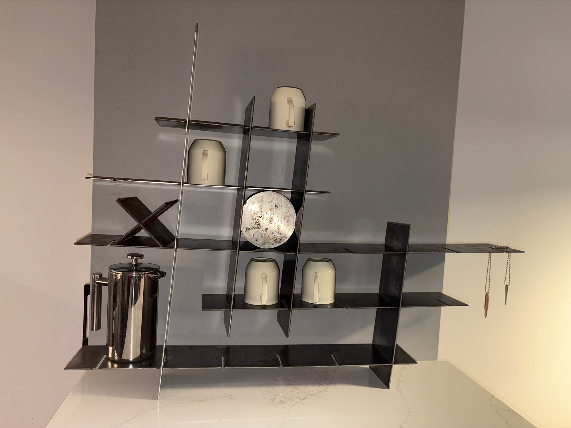 Modern black metal shelving unit with geometric grid design displaying white ceramic vessels, chubby pencil with steampunk lighter, French press, and decorative items against neutral background